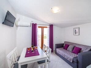 Ein Zimmer mit Esstisch, Stühlen, einer Couch und einem an der Wand befestigten Fernseher.