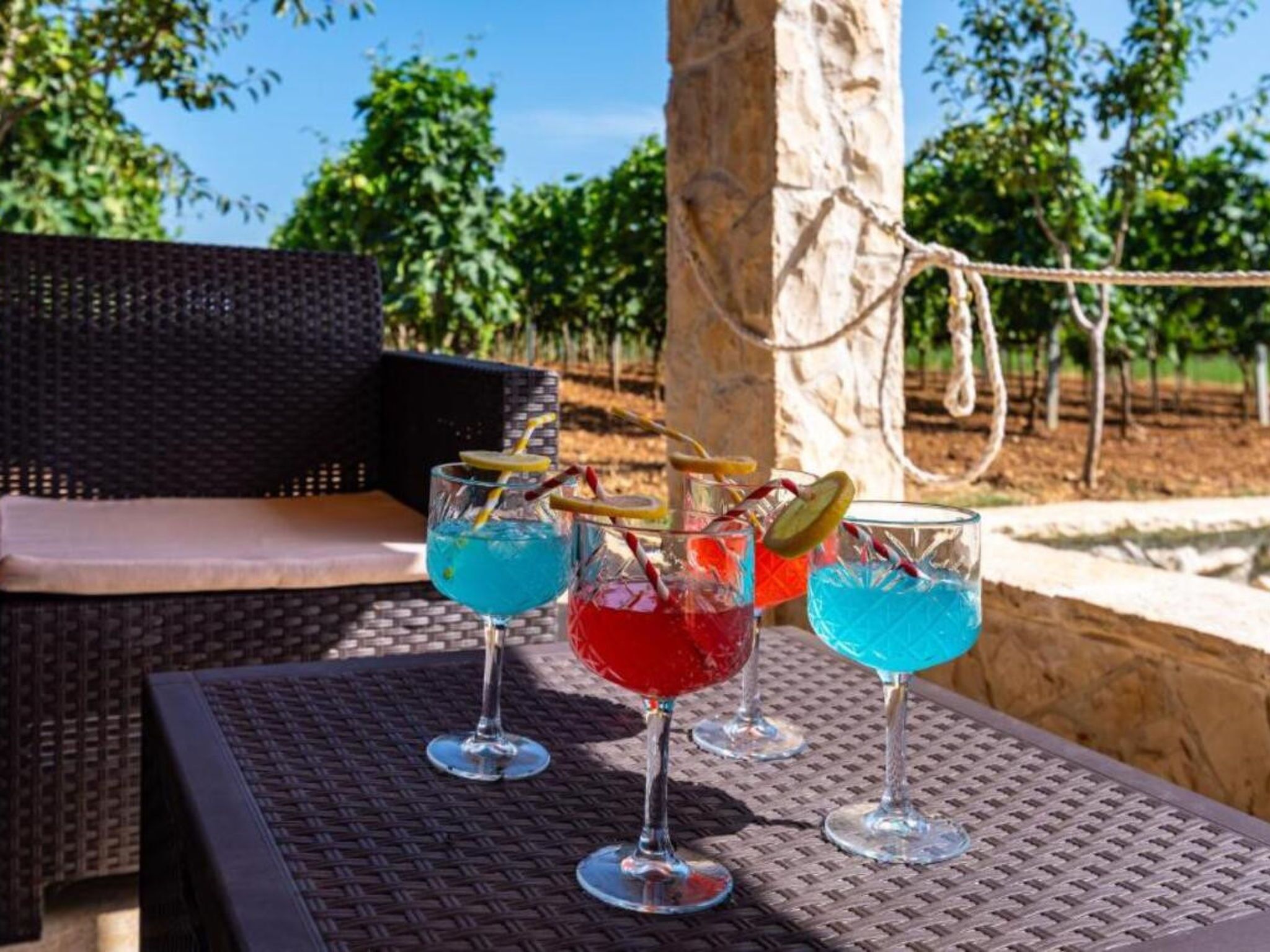 Trois verres de cocktails sont posés sur une table en fibres tressées, avec une chaise en osier et une corde en arrière-plan.
