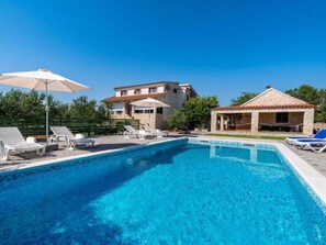 A swimming pool with lounge chairs and umbrellas, a stone building, and a smaller structure with a tiled roof. - Apartment Tonka 3+2 by Interhome (Donje Rastane)