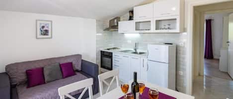 A compact living space with a kitchenette, a dining area with a table set for two, and a sofa.