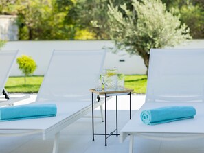 Ein Poolbereich mit Liegestühlen und einem kleinen Tisch mit Tablett, auf dem Gläser und ein Krug stehen.