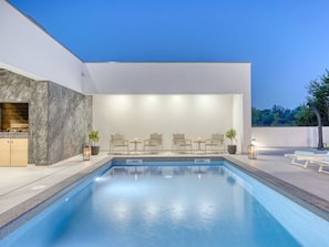 Un'area piscina moderna all'aperto con zona relax e angolo cottura.