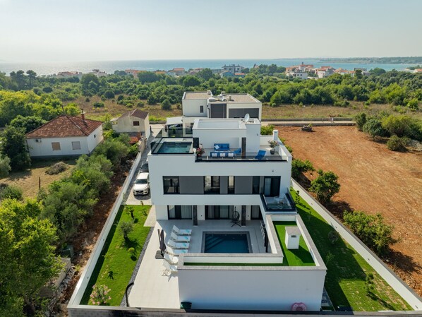 Une maison moderne à deux étages, dotée d’une piscine, d’un jardin et offrant une vue sur la mer.