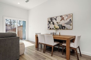 A dining area with a wooden table, four chairs, and a large abstract painting on the wall. - All New Beautiful New Build, Come and See! (Commerce)