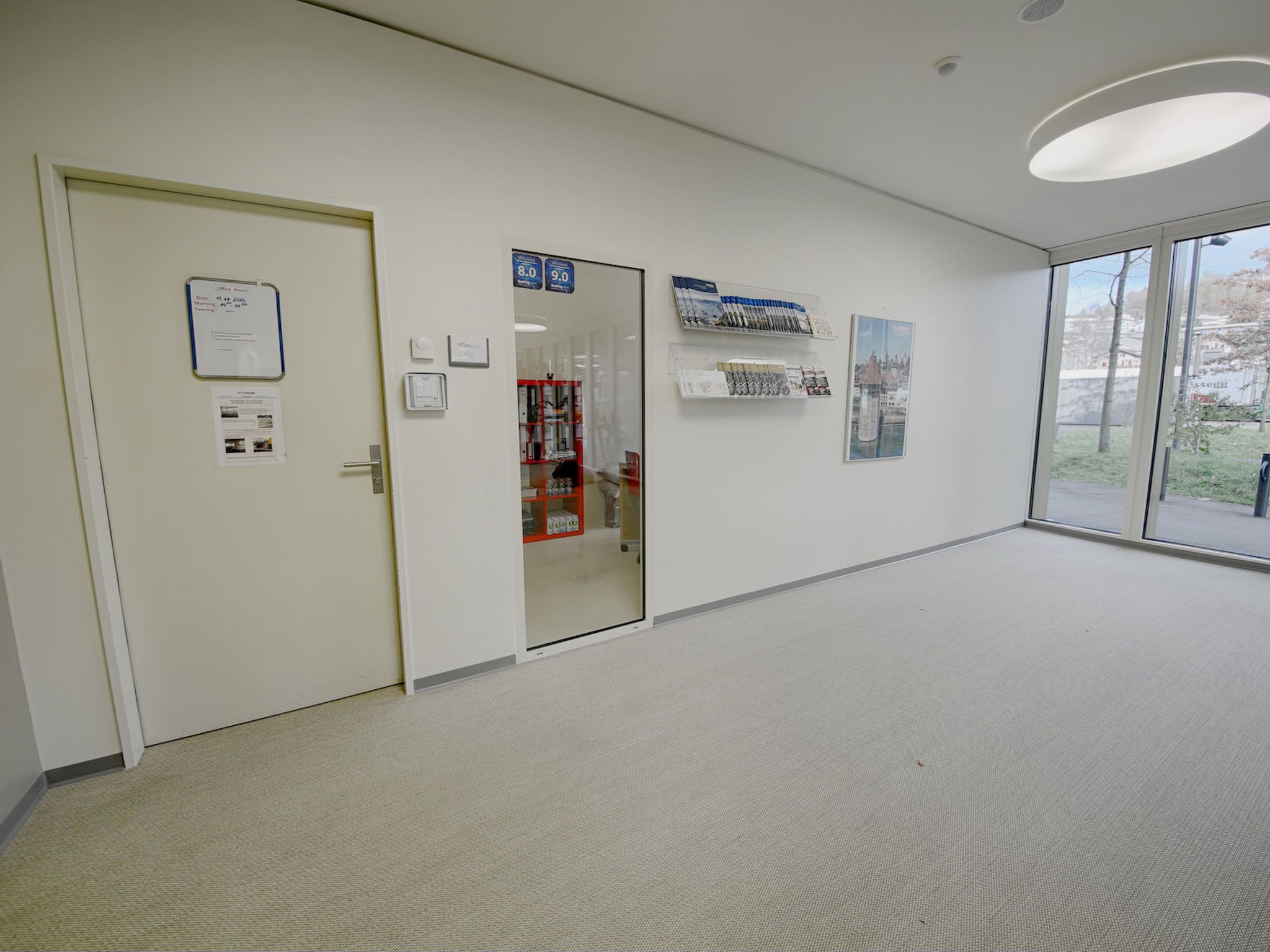A hallway with a door, a bulletin board, and a window with a view.