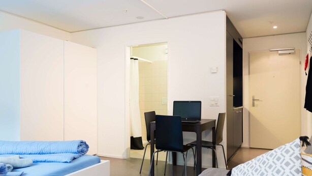 Een moderne hotelkamer met een bed, een bureau met een computer en een stoel.