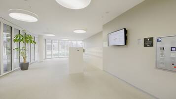 A modern, well-lit hallway with a reception desk, a mounted screen, and a control panel.