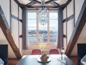 Un comedor con una mesa, sillas, una araña y un ventanal con vistas a edificios.