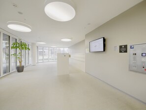 Un couloir moderne et bien éclairé, avec un comptoir d’accueil, un écran fixé au mur et un panneau de contrôle.
