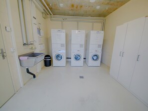 A laundry room with three stacked washing machines, a sink, and a trash bin. - Apartment  by Interhome (Lucerne)