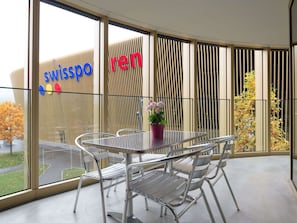 A modern interior with a glass wall, metal furniture, and a view of a building with signage. - Apartment  by Interhome (Lucerne)
