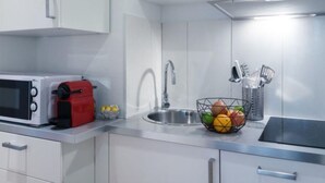 Una cocina moderna con armarios blancos, un lavamanos de acero inoxidable, un microondas, un tostador rojo y una cesta de frutas.