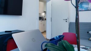 Una habitación de hotel moderna con una televisión de pantalla plana, una computadora portátil, una silla roja, una taza azul y una planta en maceta.