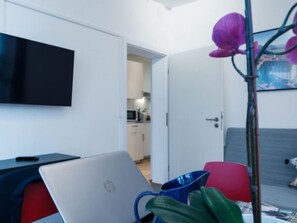 Ein modernes Hotelzimmer mit Flachbildfernseher, einem Laptop, einem roten Sessel, einer blauen Tasse und einem Blumentopf.