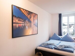 Ein Schlafzimmer mit Bett, Kissen, einem Fenster und einem Wandbild.