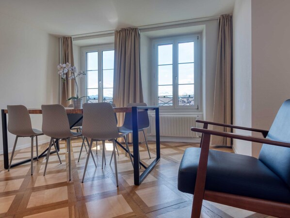 A dining area with a table and chairs, a view through a window, and a radiator. - LU Jupiter 3 - Chapel Bridge HITrental Apartment by Interhome (Lucerne)