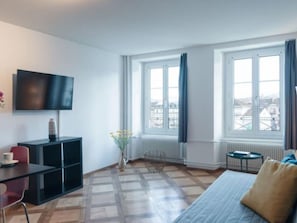 Una habitación moderna con televisor de pantalla plana, una mesita, un sofá y ventanas amplias con cortinas.