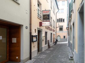 Une rue étroite bordée de bâtiments des deux côtés, dont un restaurant appelé « Schiff » et une enseigne indiquant « HIT rental ».