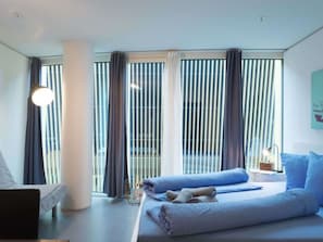 Une chambre d’hôtel moderne équipée d’un lit, de rideaux, d’une fenêtre et d’un luminaire fixé au mur.