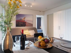 Een hotelkamer met een bed, een eettafel gedekt met een fruitschaal, een fles wijn en glazen. Op tafel staat een vaas met bloemen.