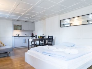 A modern hotel room with a large bed, a dining table with chairs, a kitchenette, and a large mirror on the wall. - ZG Zeughausgasse II - HITrental Apartment by Interhome (Zoug)