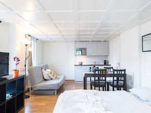 A modern hotel room with a sofa, a dining table with chairs, a kitchen area, and a TV. - ZG Zeughausgasse II - HITrental Apartment by Interhome (Zoug)