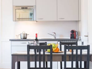 A modern kitchen with white cabinets, a built-in oven, a sink, and a dining area with a table and chairs. - ZG Zeughausgasse II - HITrental Apartment by Interhome (Zoug)