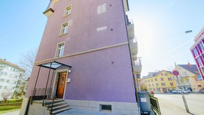 En bygning med flere etager, en lilla facade, en trædør og en lille trappe op til indgangen.