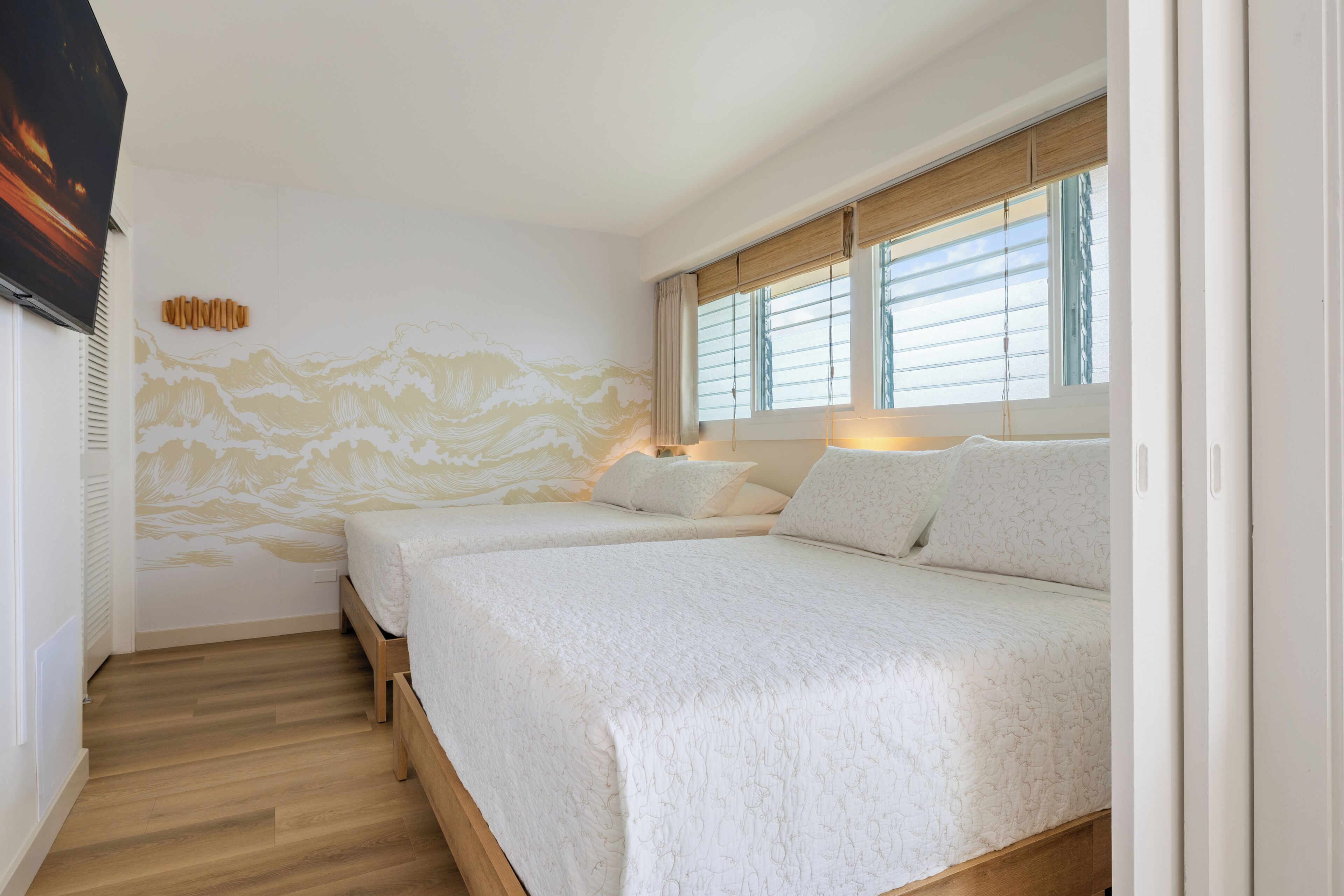 Een slaapkamer met twee bedden, een houten vloer, een wanddecoratie en een raam met jaloezieën.