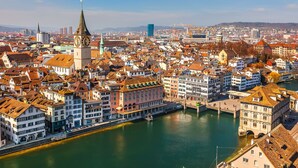 Una vista panorámica de una ciudad histórica con una torre destacada y un río que la atraviesa.