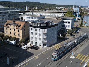 Eine Straßenbahnhaltestelle mit einem modernen Gebäude, einer Straßenbahn und einer freien Fahrbahn.