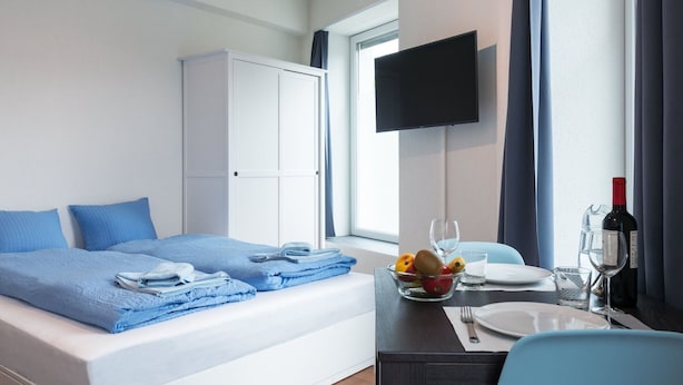 Habitación de hotel con cama, escritorio con silla, televisor y ventana con cortinas.