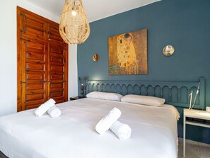 Een slaapkamer met een groot bed, een houten kledingkast, een schilderij aan de muur en een nachtkastje met een lamp.
