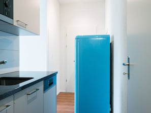 Pieni, käytännöllinen keittiö, jossa on sininen jääkaappi, pesuallas ja kaapistot.