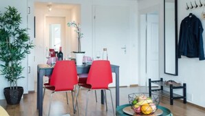 Ein modernes Wohnzimmer mit Essbereich, einem Blumentopf, einer Obstschale und einem Garderobeständer.