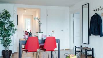 Un salon moderne comprenant un coin repas, une plante en pot, un panier de fruits et un porte-manteau.