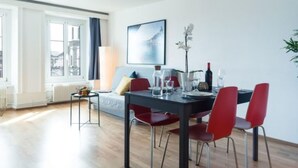 Ein moderner Essbereich mit Tisch, Stühlen und Blick auf die Stadt durch große Fenster.