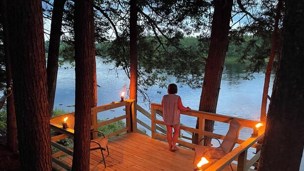 A wooden deck with railings overlooking a body of water, surrounded by trees. -  1-bedroom off grid cabin in serene Woodville perfect for relaxing getaway (Woodville)