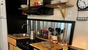 A compact kitchen with a stove, sink, and wooden cabinets. -  1-bedroom off grid cabin in serene Woodville perfect for relaxing getaway (Woodville)