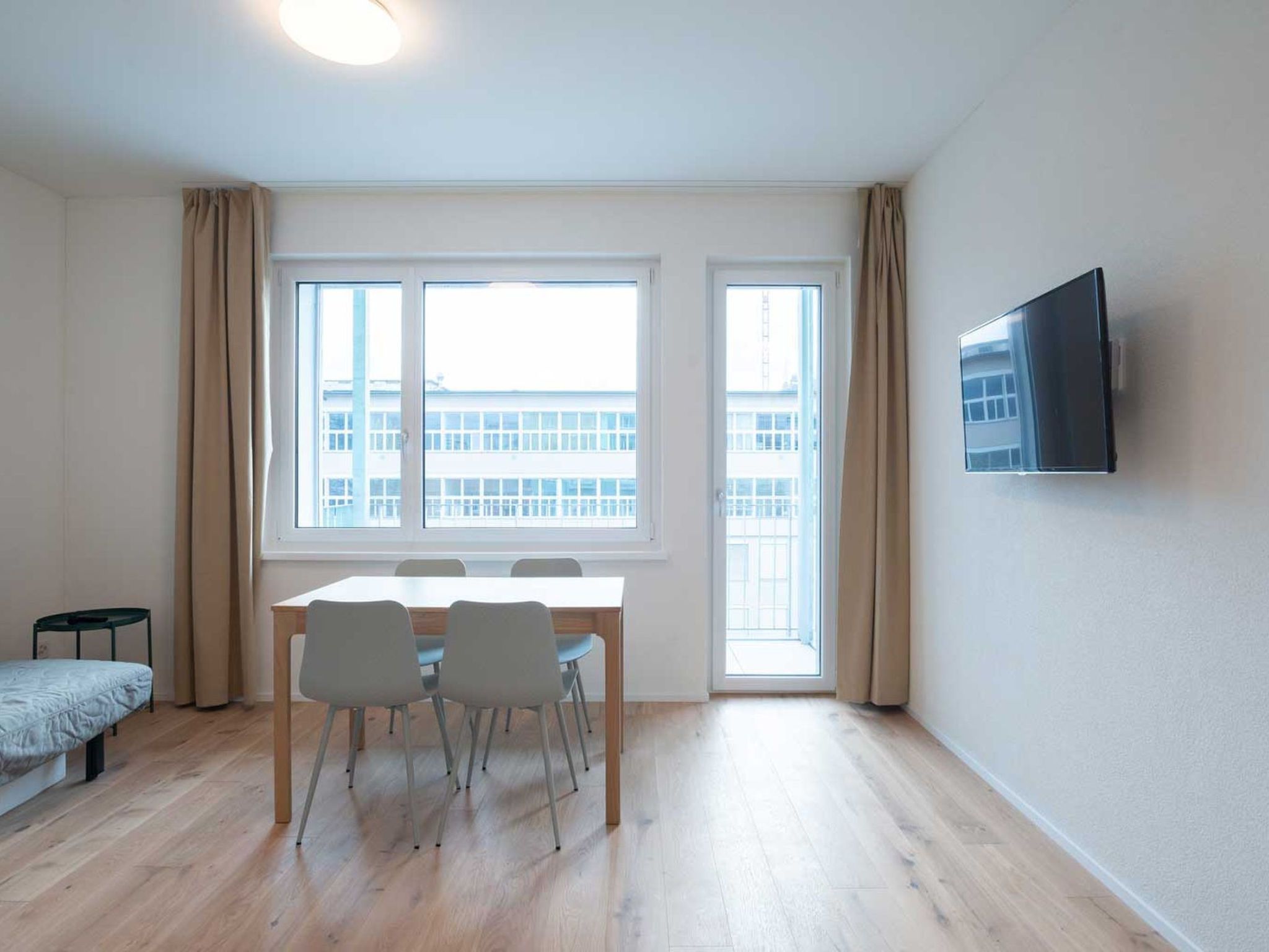 Een moderne, goed verlichte kamer met een eettafel, stoelen, een bank en een aan de muur bevestigde televisie.