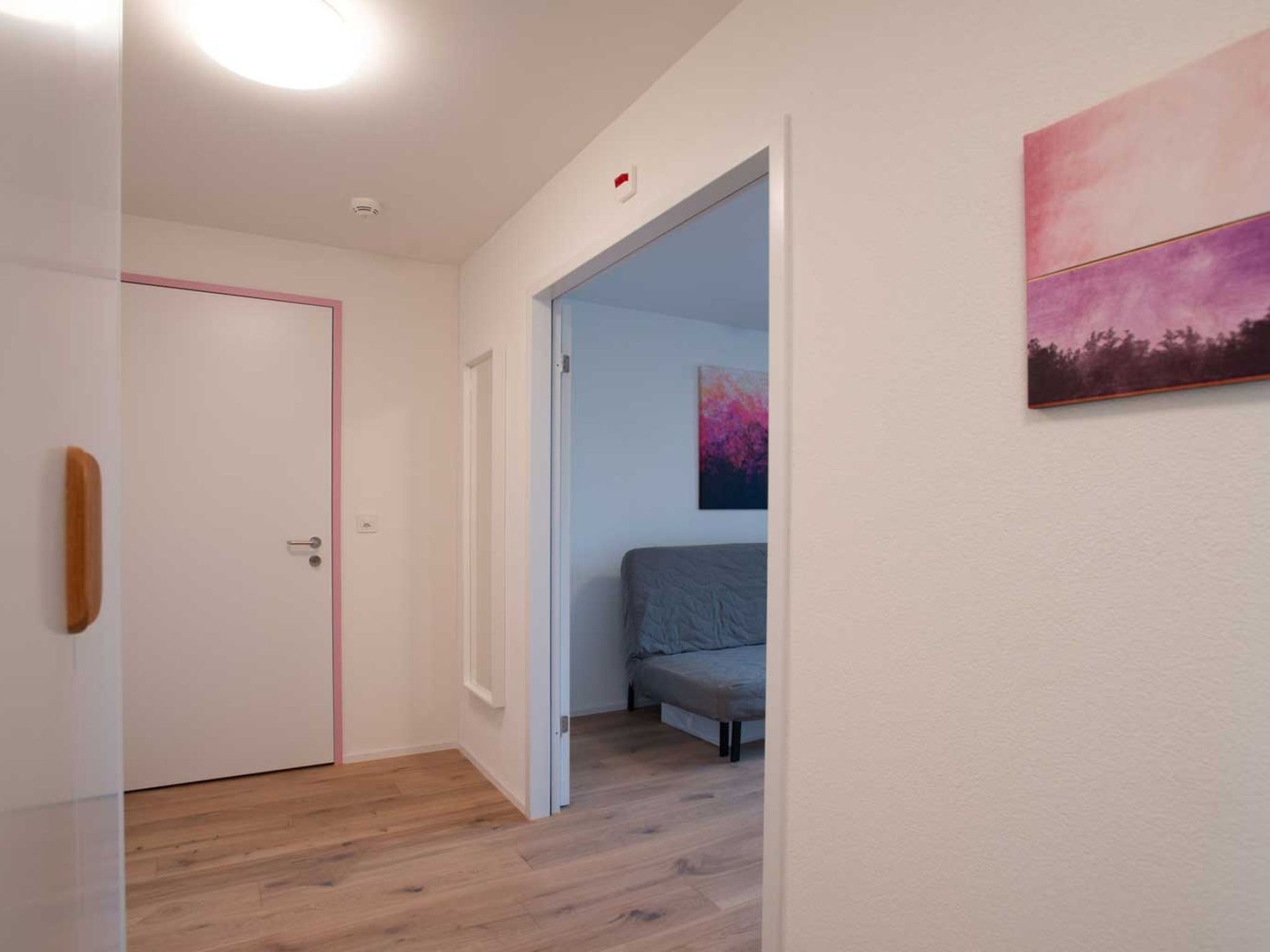 Un pasillo con una puerta, una cama en la habitación contigua y un cuadro en la pared.