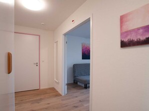 Un passadís amb una porta, un llit a la habitació següent i un quadre a la paret.