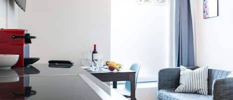 Una cocina moderna con un electrodoméstico rojo, una mesa de comedor con un cuenco de fruta y un sofá gris con un cojín estampado.