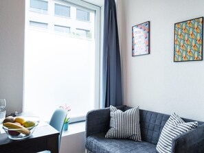 Una sala de estar moderna con un sofá gris, una mesa de vidrio con frutas y una ventana con cortinas.