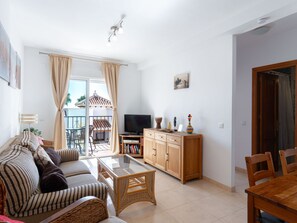 Un salon avec un canapé, un téléviseur, un meuble en bois et un balcon donnant sur un immeuble.
