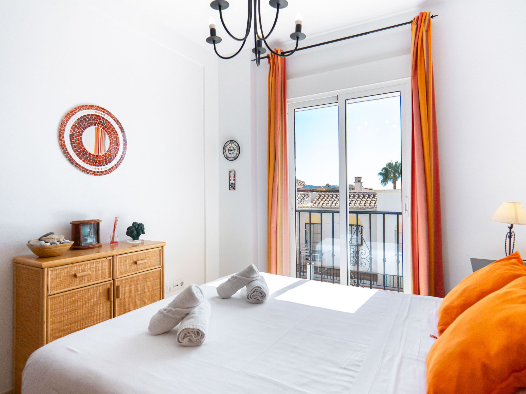 Een hotelkamer met een bed, een dressoir, een spiegel en een balkon met oranje gordijnen.