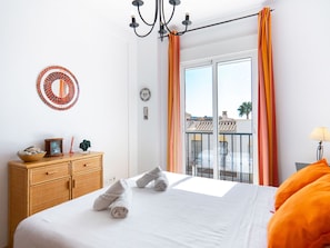 Quarto de hotel com cama, cômoda, espelho e varanda com cortinas laranja.