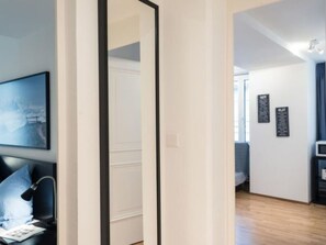 Une chambre d’hôtel avec un lit, un bureau doté d’une lampe, un tableau au mur et une vue sur le couloir.