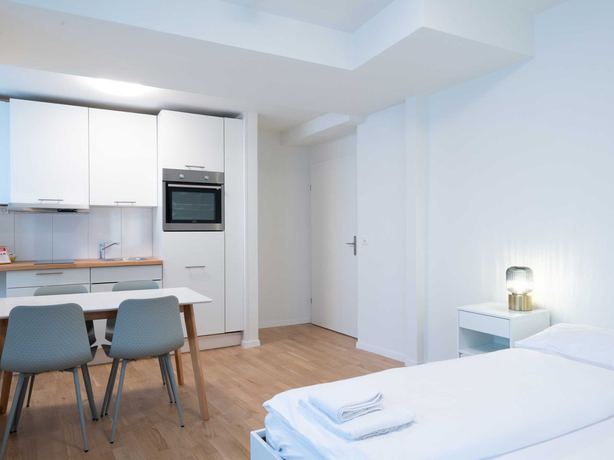 Ein modernes, minimalistisches Hotelzimmer mit Bett, Nachttisch und einer kleinen Arbeitsfläche mit Stühlen.