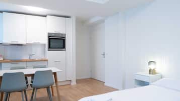Een moderne, minimalistisch ingerichte hotelkamer met een bed, nachtkastje en een klein werkgedeelte met stoelen.